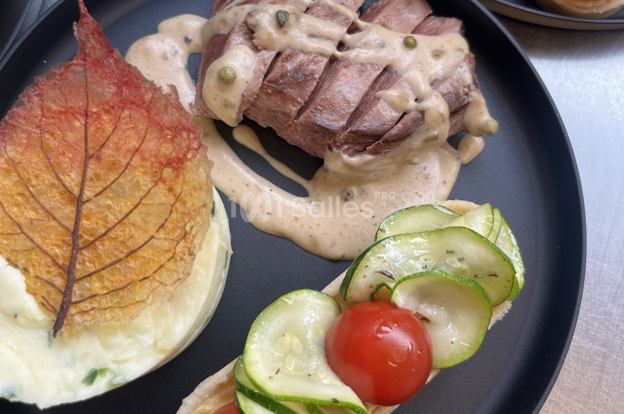 Assiette composée d'un steak nappé de sauce, purée décorée d'une feuille croustillante et garniture de légumes frais.