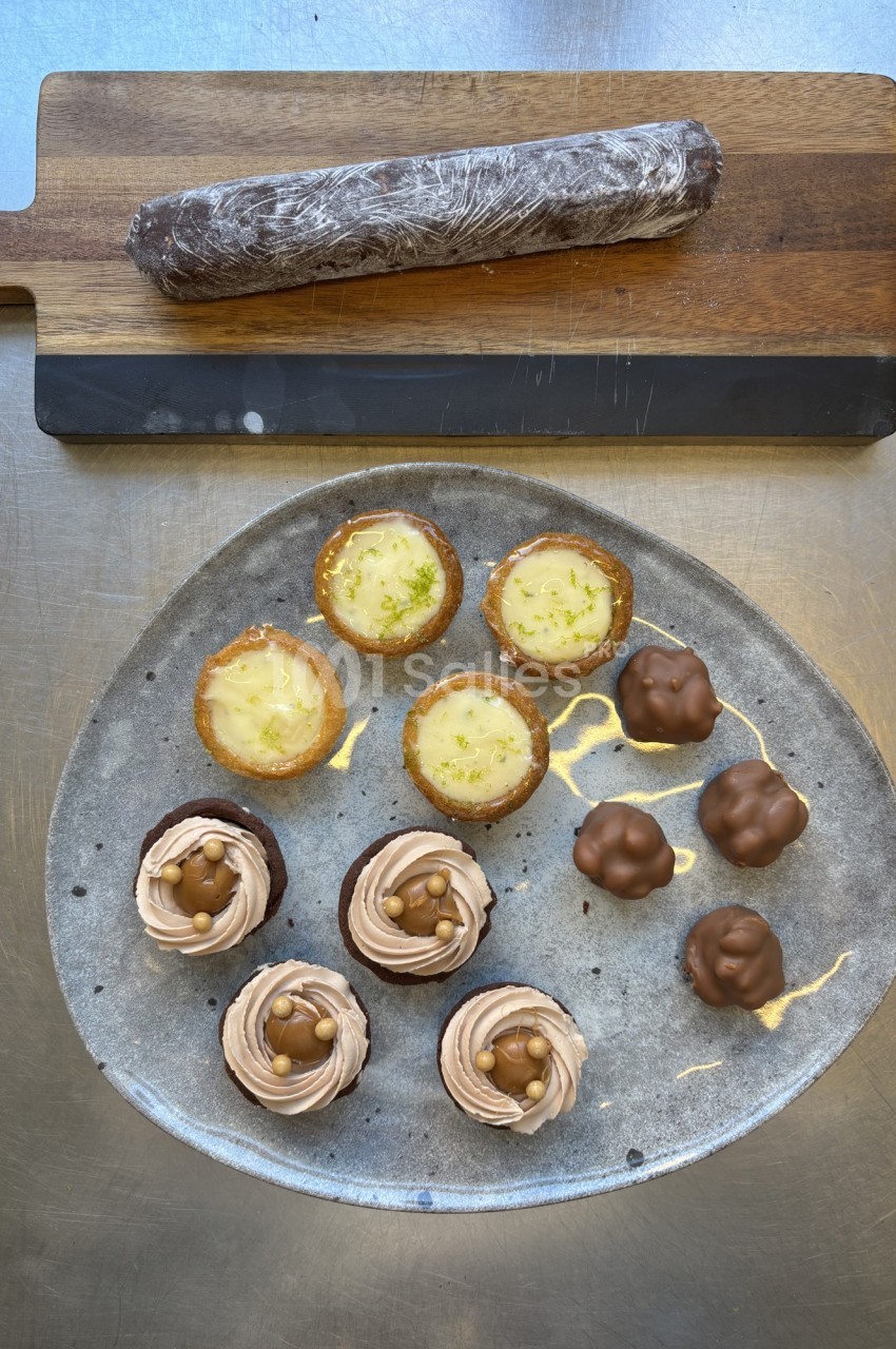 Assortiment de desserts sur une assiette : tartelettes, cupcakes au chocolat et bouchées enrobées, avec un roulé au chocolat.