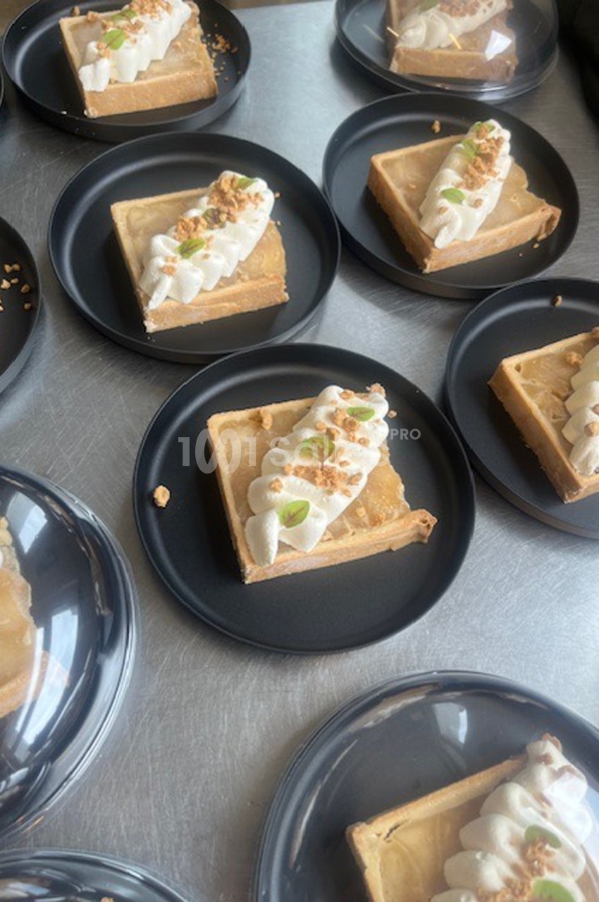 Parts de tarte garnies de crème fouettée, éclats de noix et zestes, présentées sur des assiettes noires.