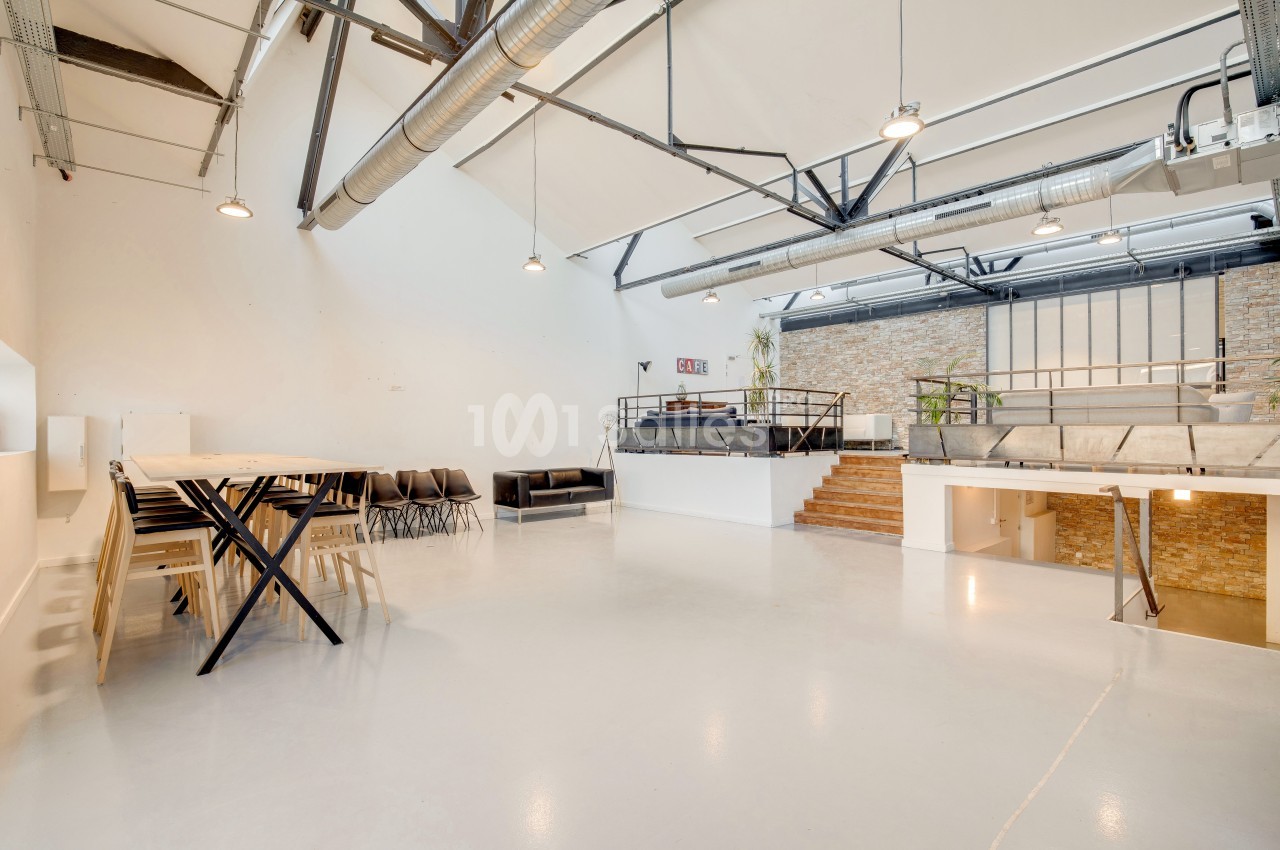 Espace intérieur lumineux avec mezzanine, murs en briques, grandes poutres apparentes et mobilier minimaliste.
