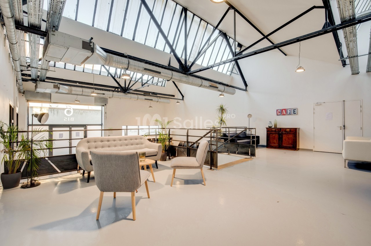Espace lumineux avec mobilier moderne, plantes et verrière, aménagé dans un style industriel épuré.