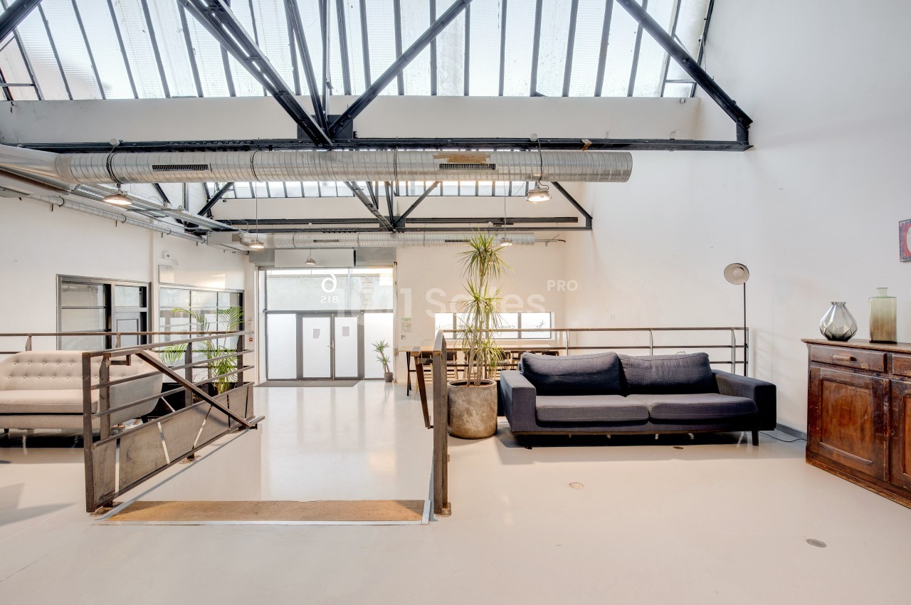 Espace lumineux avec verrière, canapé, plantes et mobilier industriel dans un intérieur moderne.