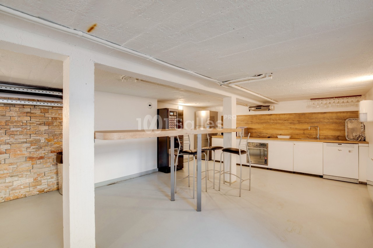 Espace ouvert avec bar haut, tabourets, coin cuisine équipé et mur en briques apparentes.