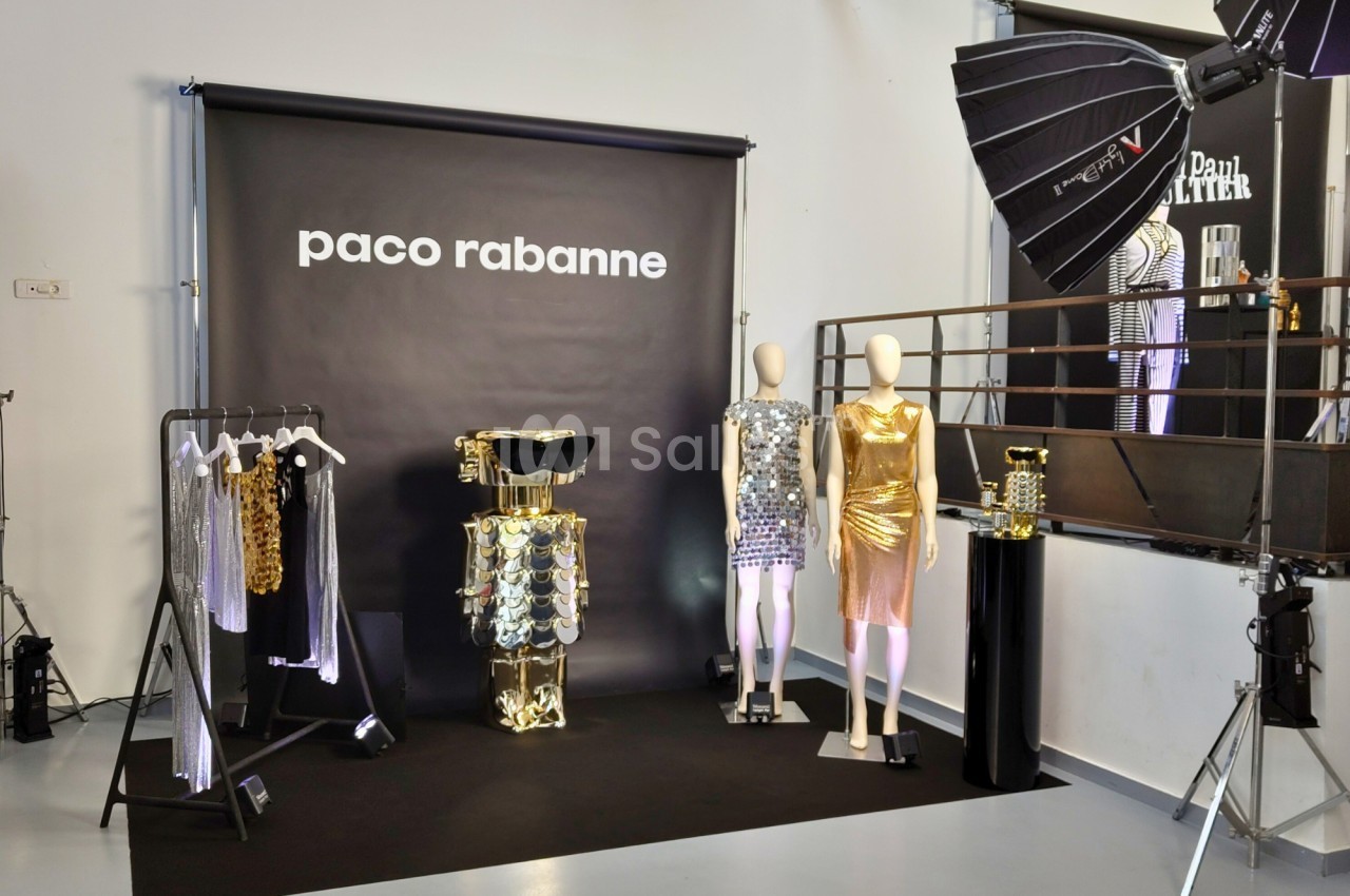 Mannequins et vêtements métallisés exposés devant un fond noir avec le logo Paco Rabanne, éclairage de studio.