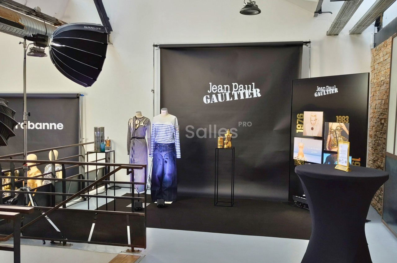 Espace d'exposition avec vêtements sur mannequins, affiches et présentoirs sous éclairage studio.