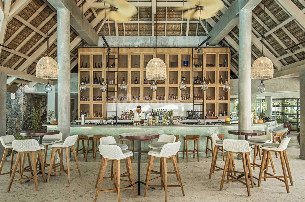 Bar moderne avec comptoir en marbre, étagères en bois remplies de bouteilles, et chaises hautes dans un espace lumineux.