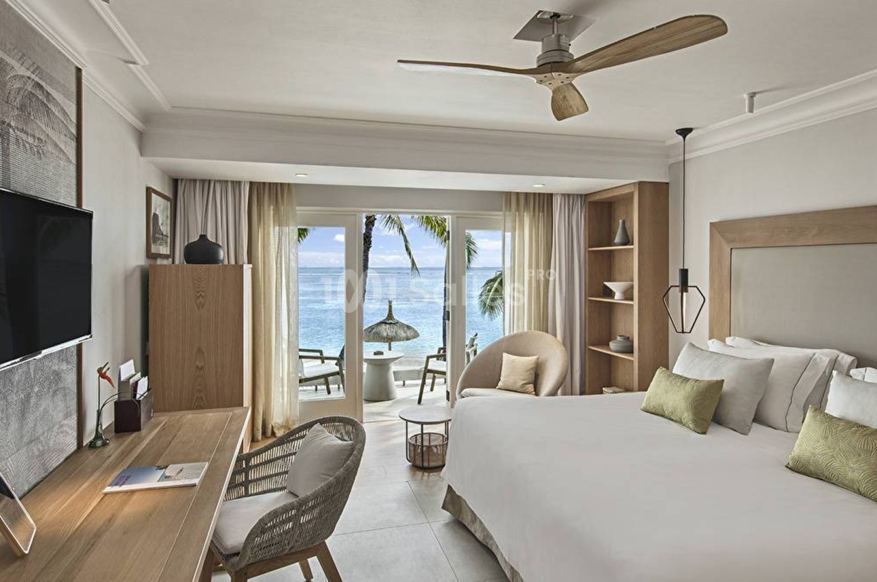 Chambre lumineuse avec lit double, bureau, télévision, et vue sur la mer à travers une baie vitrée.