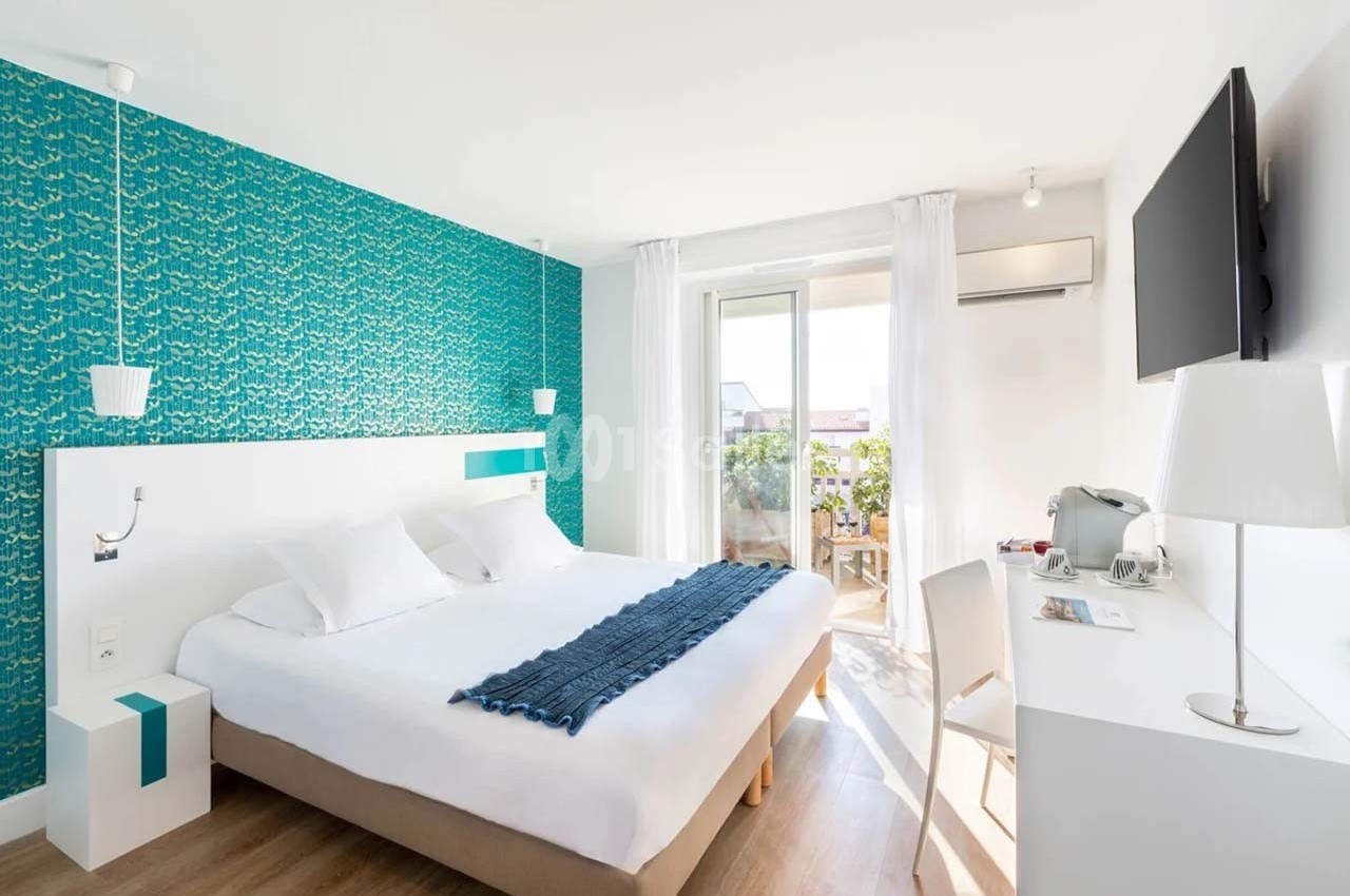 Chambre lumineuse avec lit double, bureau, télévision murale, balcon et décoration murale turquoise.