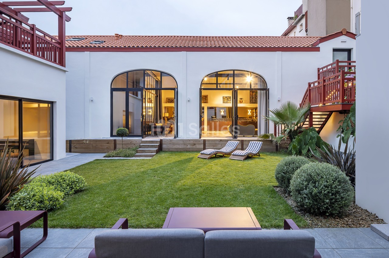 Cour intérieure avec pelouse, transats, plantes et grandes baies vitrées donnant sur un espace intérieur lumineux.