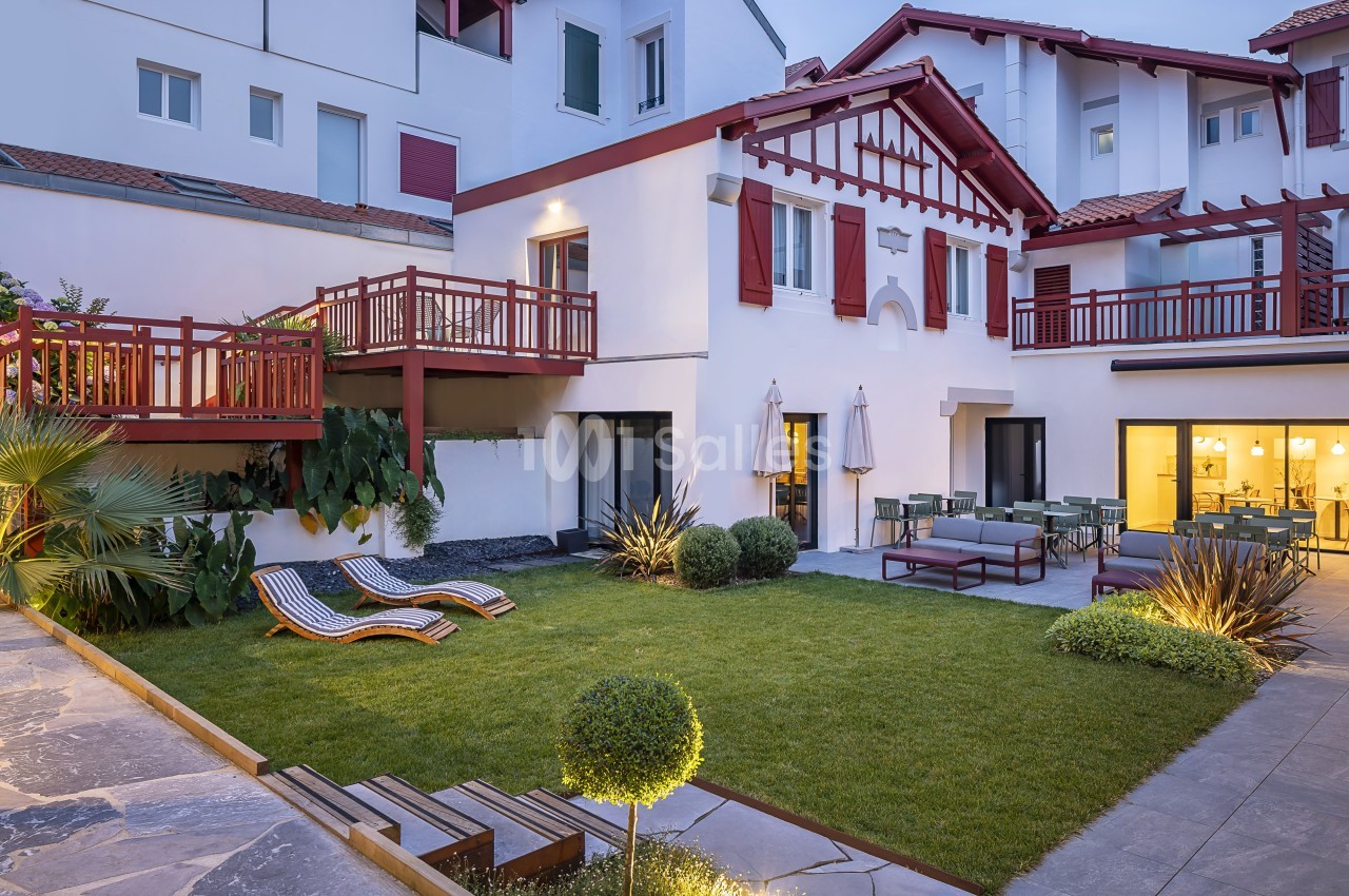 Cour intérieure avec pelouse, transats, mobilier de jardin et façades de maisons blanches à volets rouges.