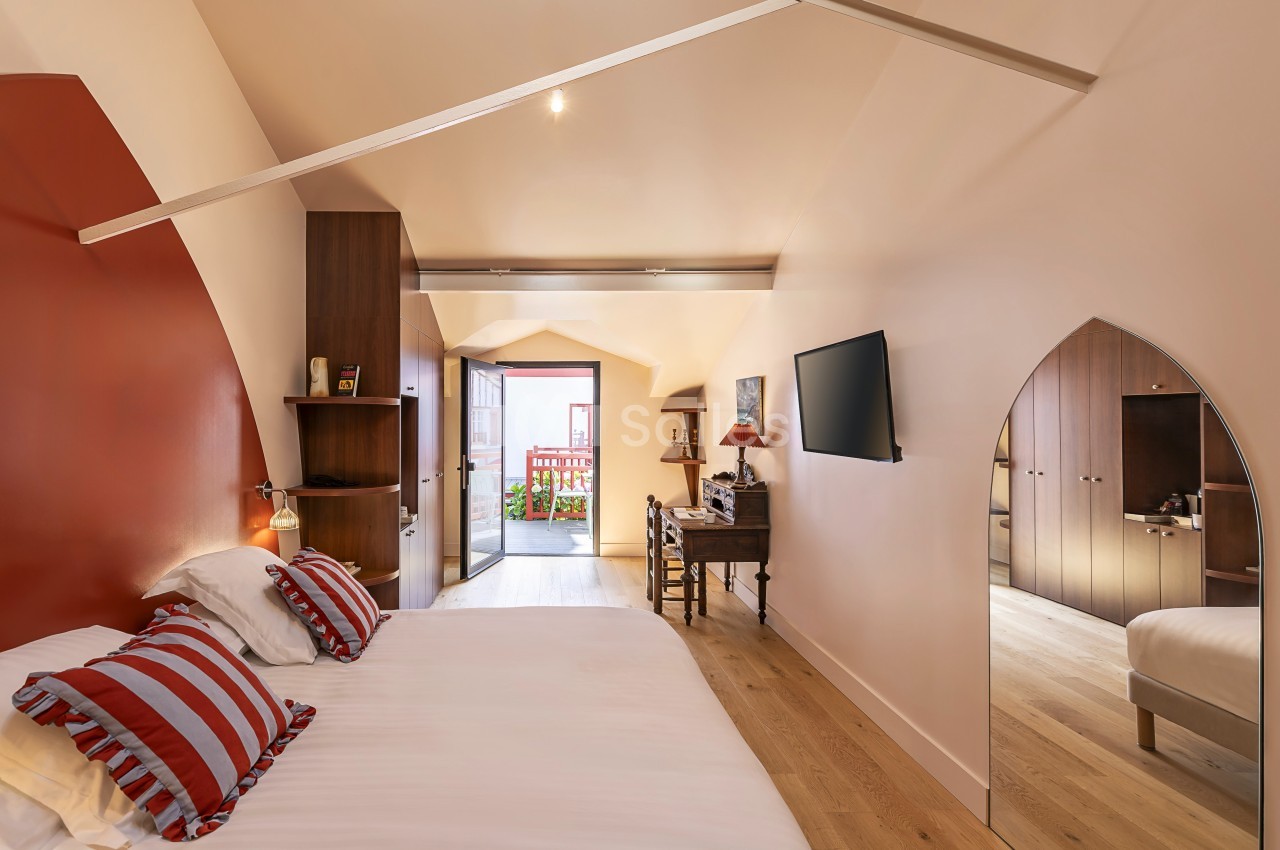 Chambre lumineuse avec lit double, bureau, télévision murale et accès à un balcon, décorée dans des tons chauds.