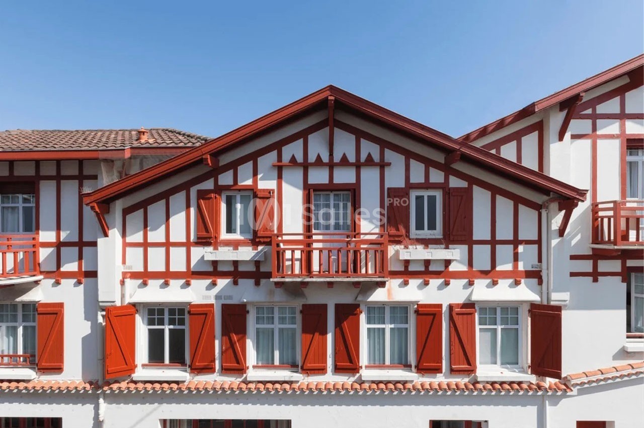Façade d'une maison traditionnelle basque blanche avec des volets et des éléments en bois rouge.
