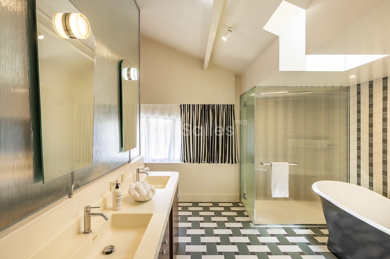 Salle de bain moderne avec double vasque, baignoire sur pied, douche vitrée et carrelage géométrique au sol.