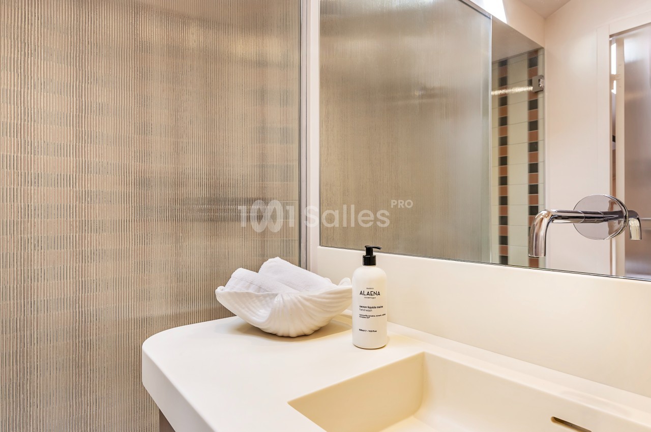 Lavabo moderne avec un distributeur de savon blanc et une serviette pliée dans une salle de bain lumineuse.