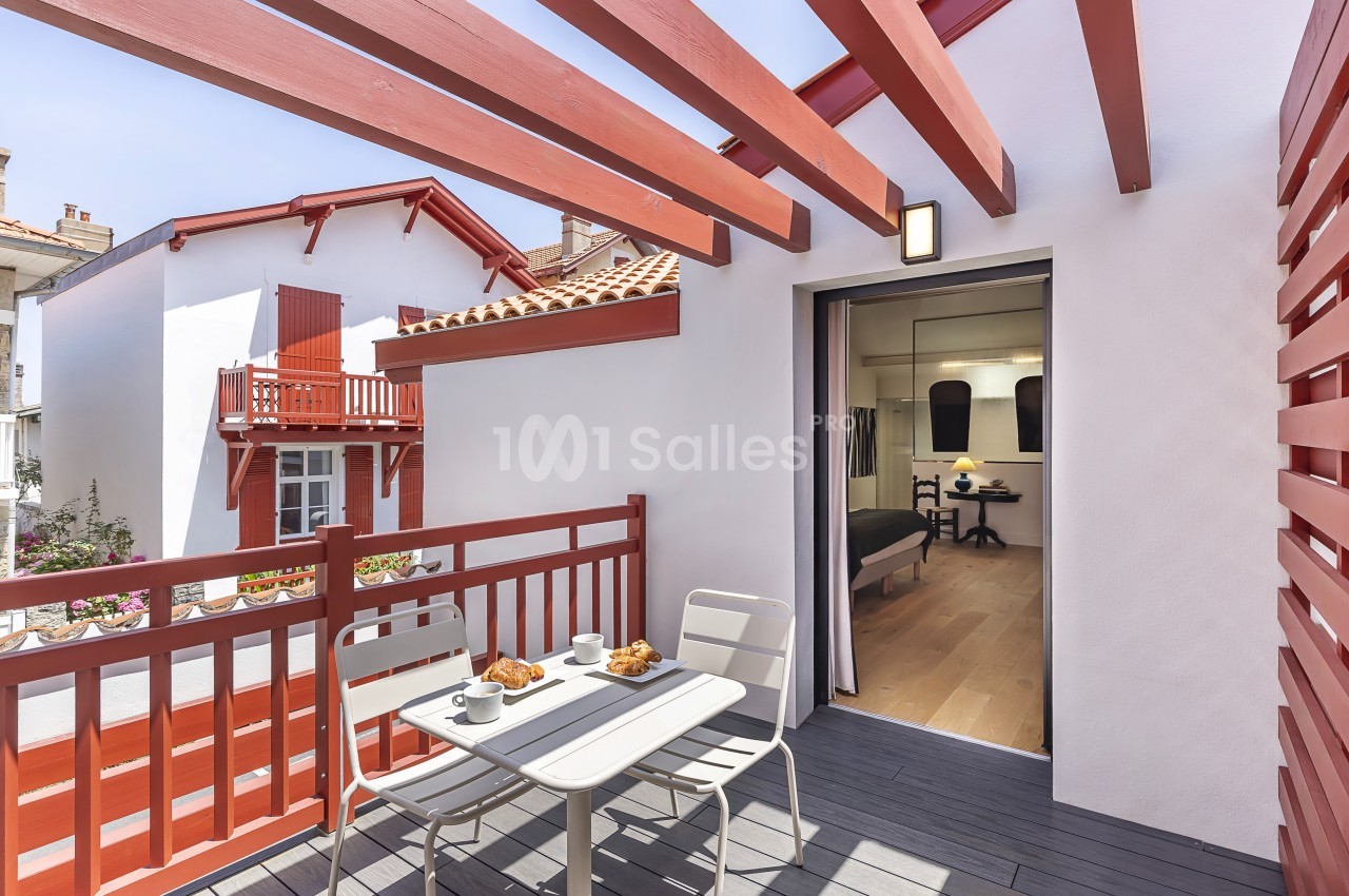 Balcon avec table et chaises, petit-déjeuner servi, vue sur des maisons blanches et rouges sous un ciel dégagé.
