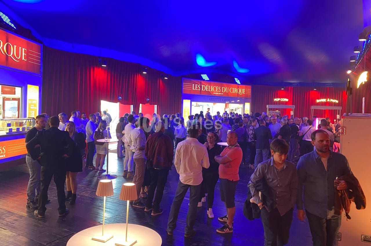 Foule rassemblée dans un chapiteau éclairé, près de stands de restauration et de boissons.