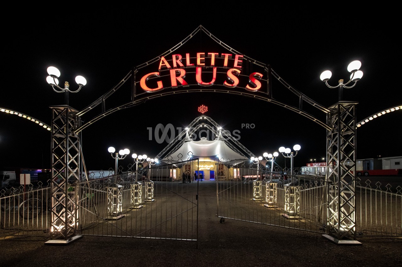 Entrée illuminée d'un chapiteau de cirque avec une arche métallique portant l'inscription ’Arlette Gruss’.