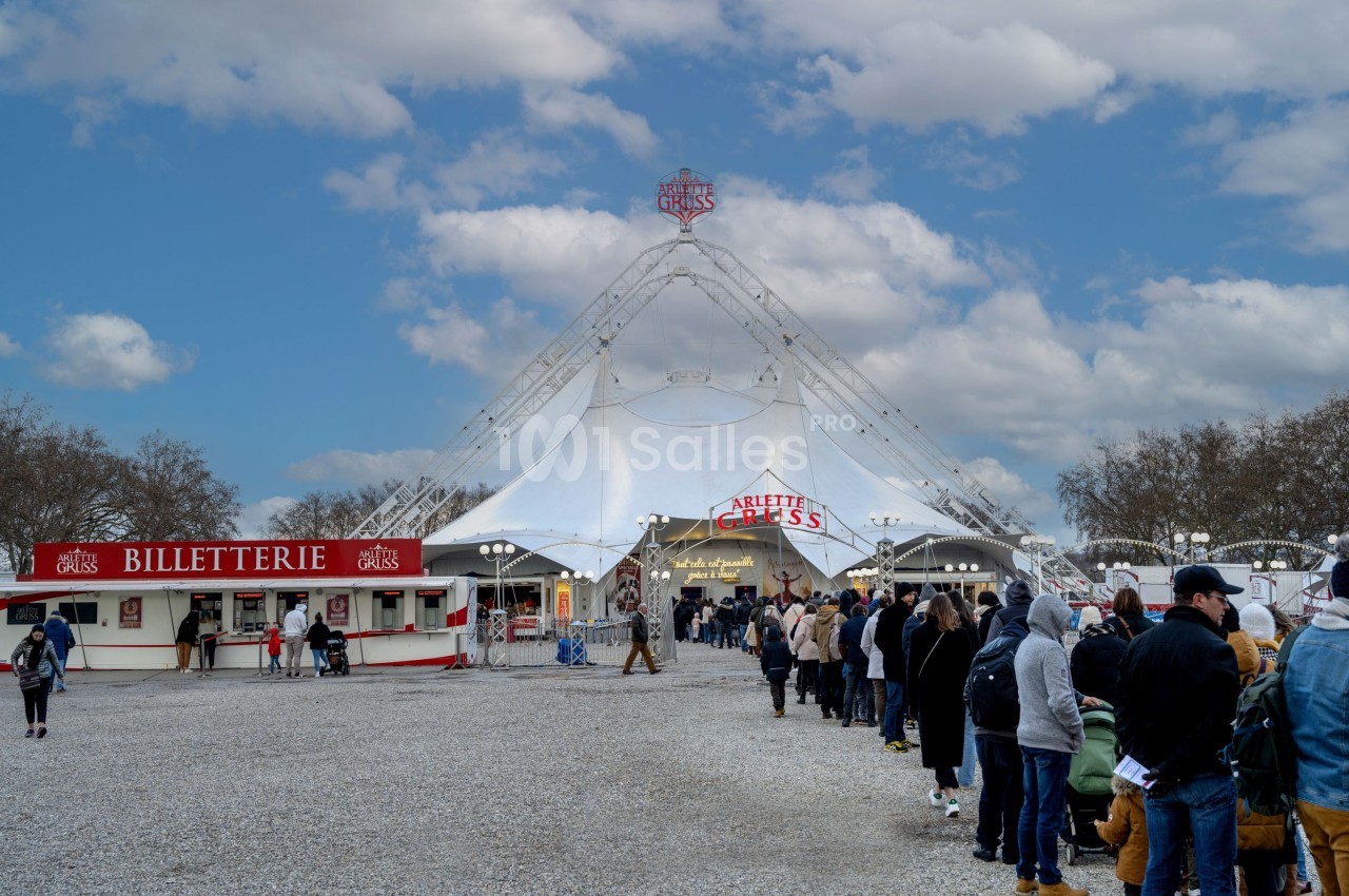 File d'attente devant un chapiteau de cirque blanc avec un guichet de billetterie sur la gauche.