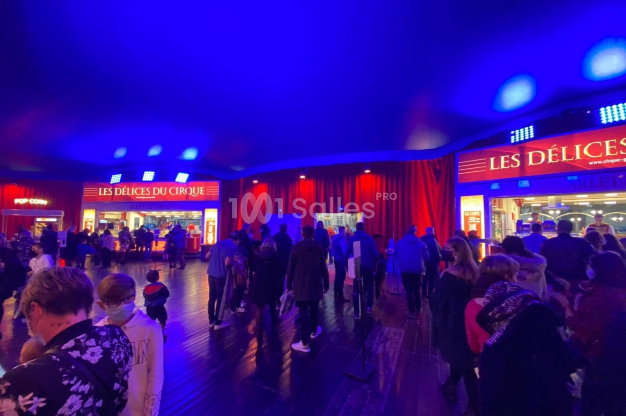 Foule rassemblée sous un chapiteau éclairé en bleu, devant des stands lumineux de restauration.