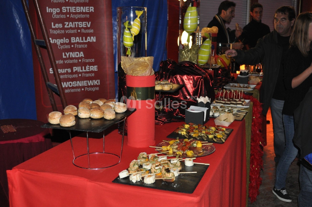 Buffet coloré avec divers amuse-bouches, brochettes et pains sur une table rouge, décorée pour un événement festif.
