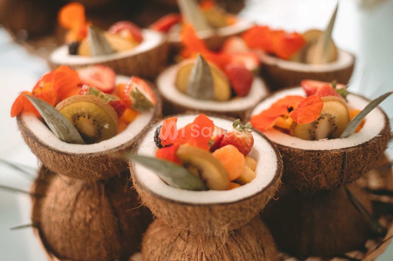 Moitiés de noix de coco remplies de fruits frais et décorées de fleurs comestibles colorées.
