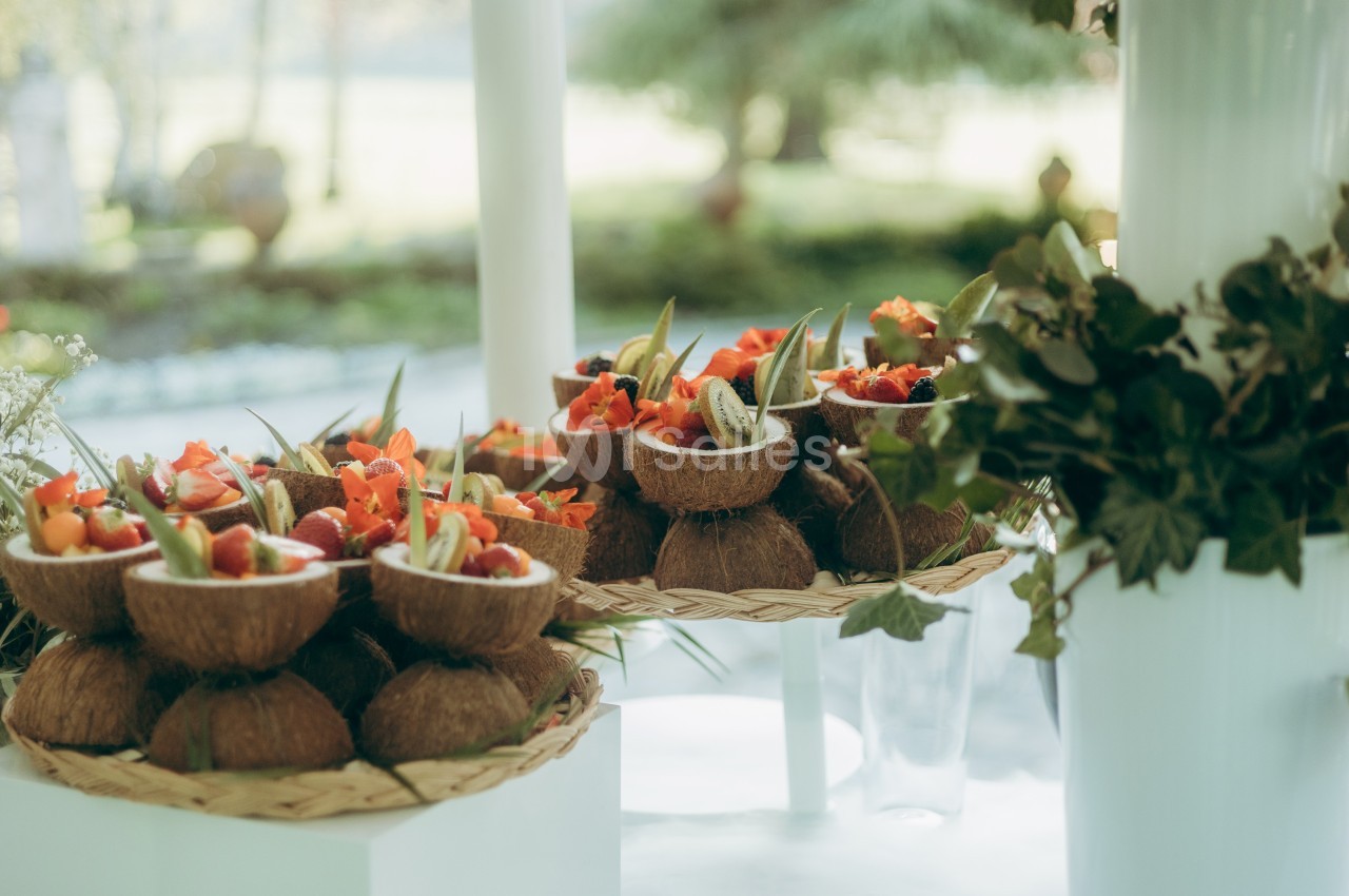 Des bols en noix de coco remplis de fruits frais et colorés, disposés sur des plateaux tressés en extérieur.