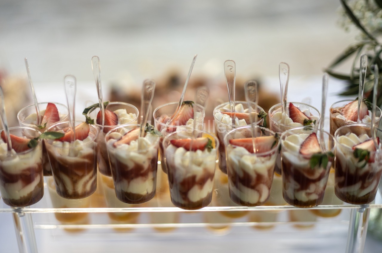 Verrines de dessert avec mousse blanche, coulis de fruits rouges et morceaux de fraises, servies avec des cuillères.