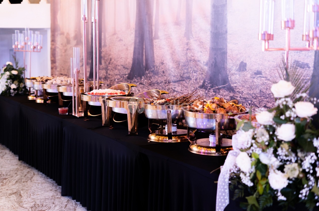 Buffet élégant avec plats variés disposés sur une table noire, décorée de fleurs blanches et chandeliers.