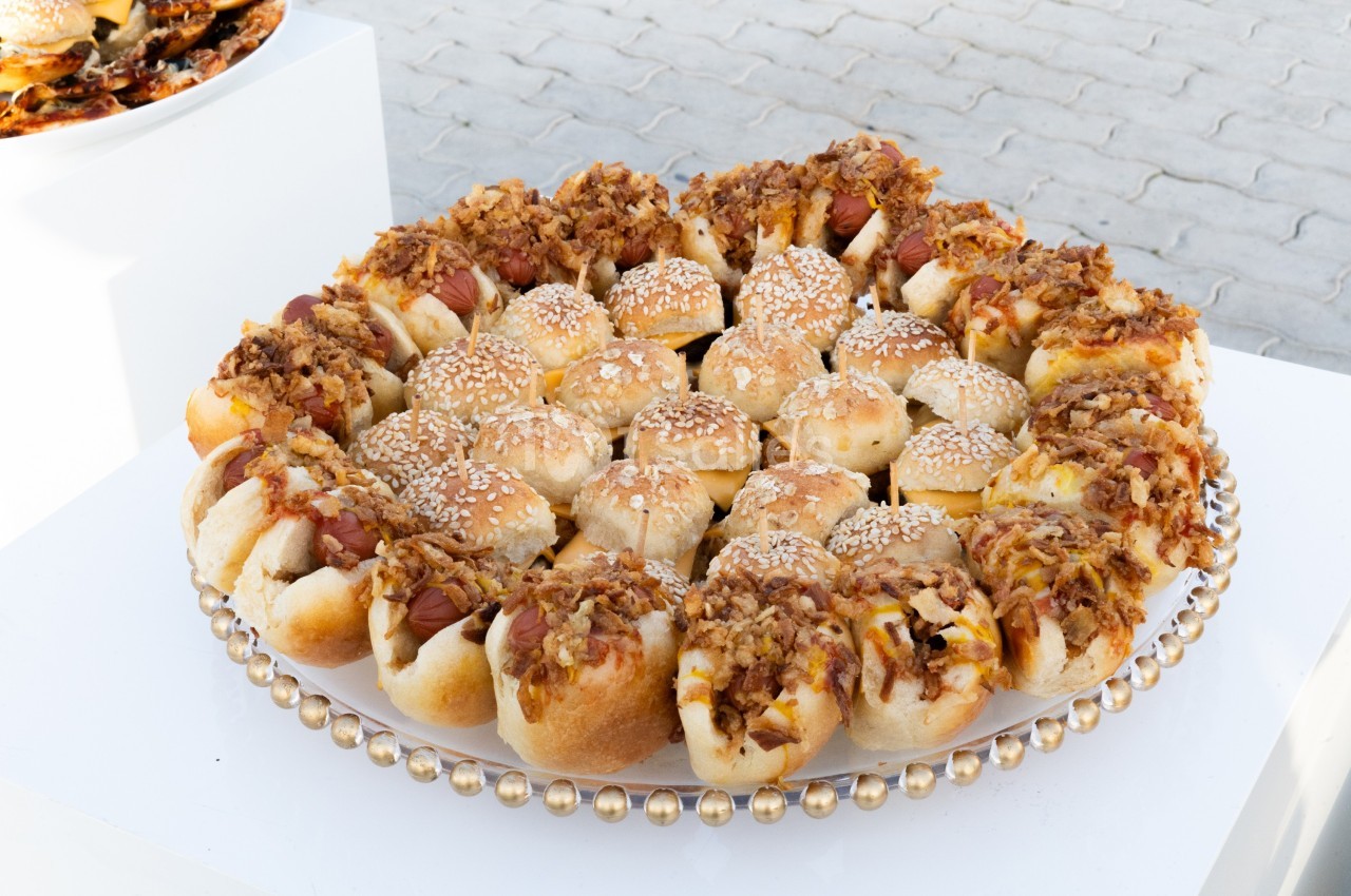 Plateau de petits pains garnis de saucisses, fromage fondu, oignons caramélisés et graines de sésame.