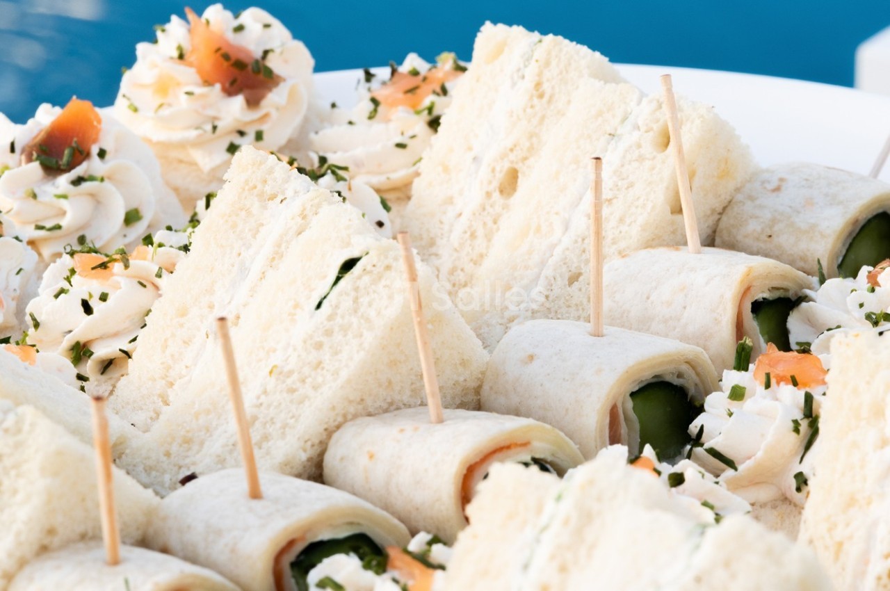 Assortiment de sandwichs roulés et triangles garnis, présentés sur un plateau avec des décorations fraîches.