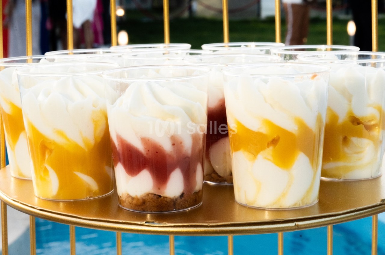 Verrines de desserts avec mousse blanche, coulis de fruits rouges et jaunes, présentées sur un plateau doré.