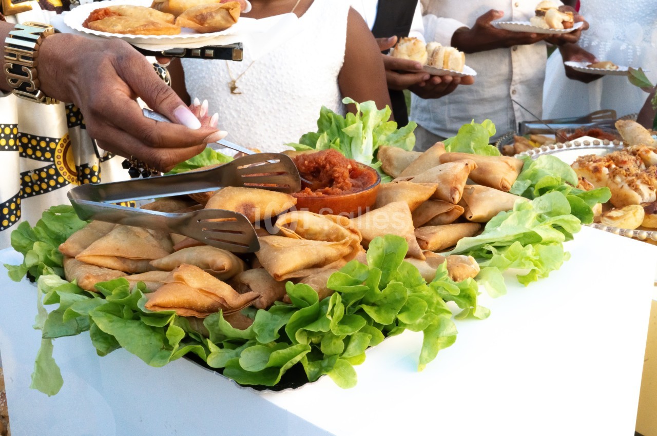 Plateau de samoussas disposés sur un lit de laitue, accompagnés d'une sauce rouge au centre, servi lors d'un buffet.