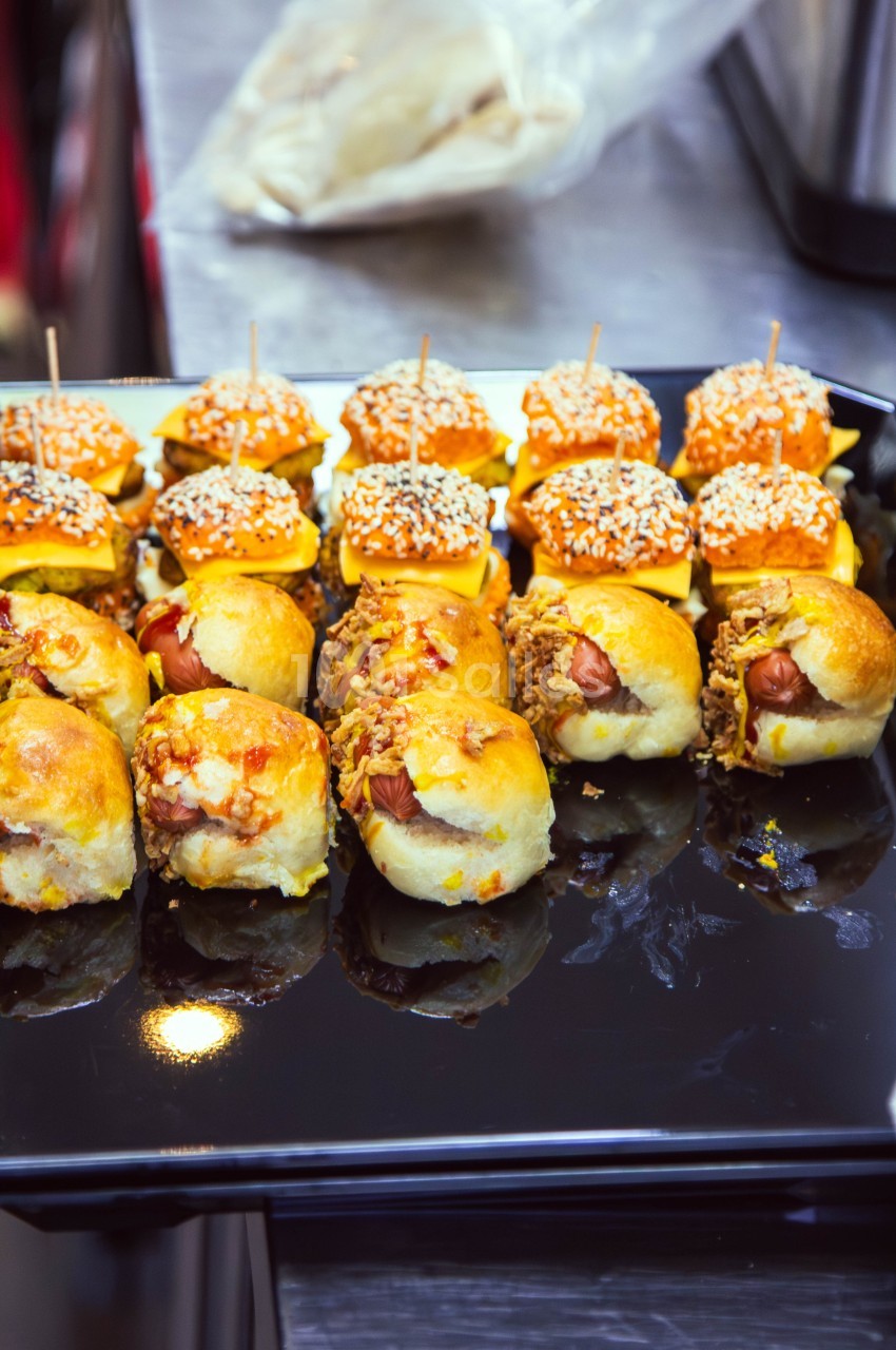 Plateau de mini-sandwichs variés, garnis de saucisses, fromage, viande effilochée et graines de sésame.