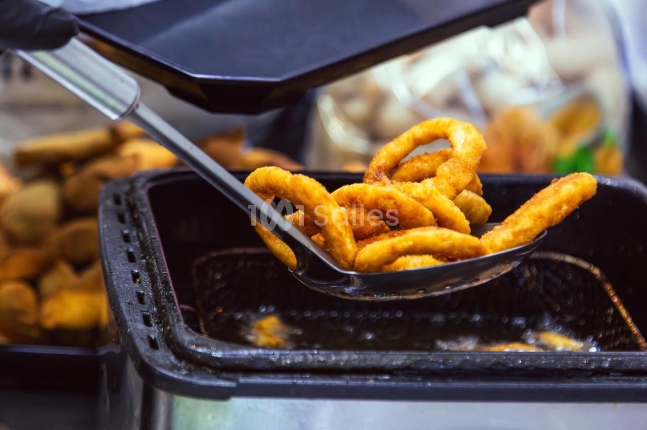 Anneaux d'oignon frits dorés sortis d'une friteuse à l'aide d'une écumoire noire.