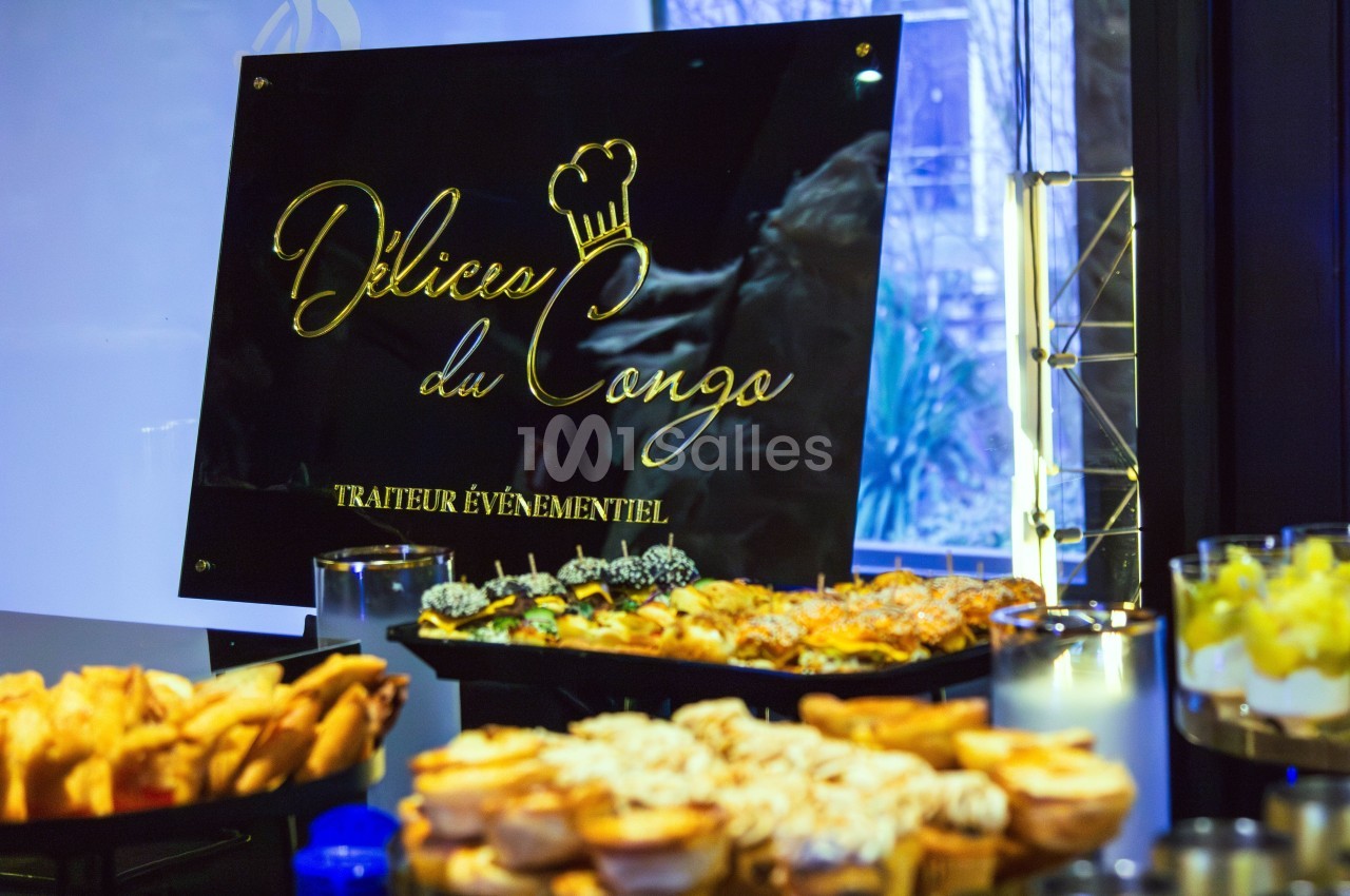 Buffet avec des plats variés devant un panneau noir indiquant ’Délices du Congo, traiteur événementiel’.