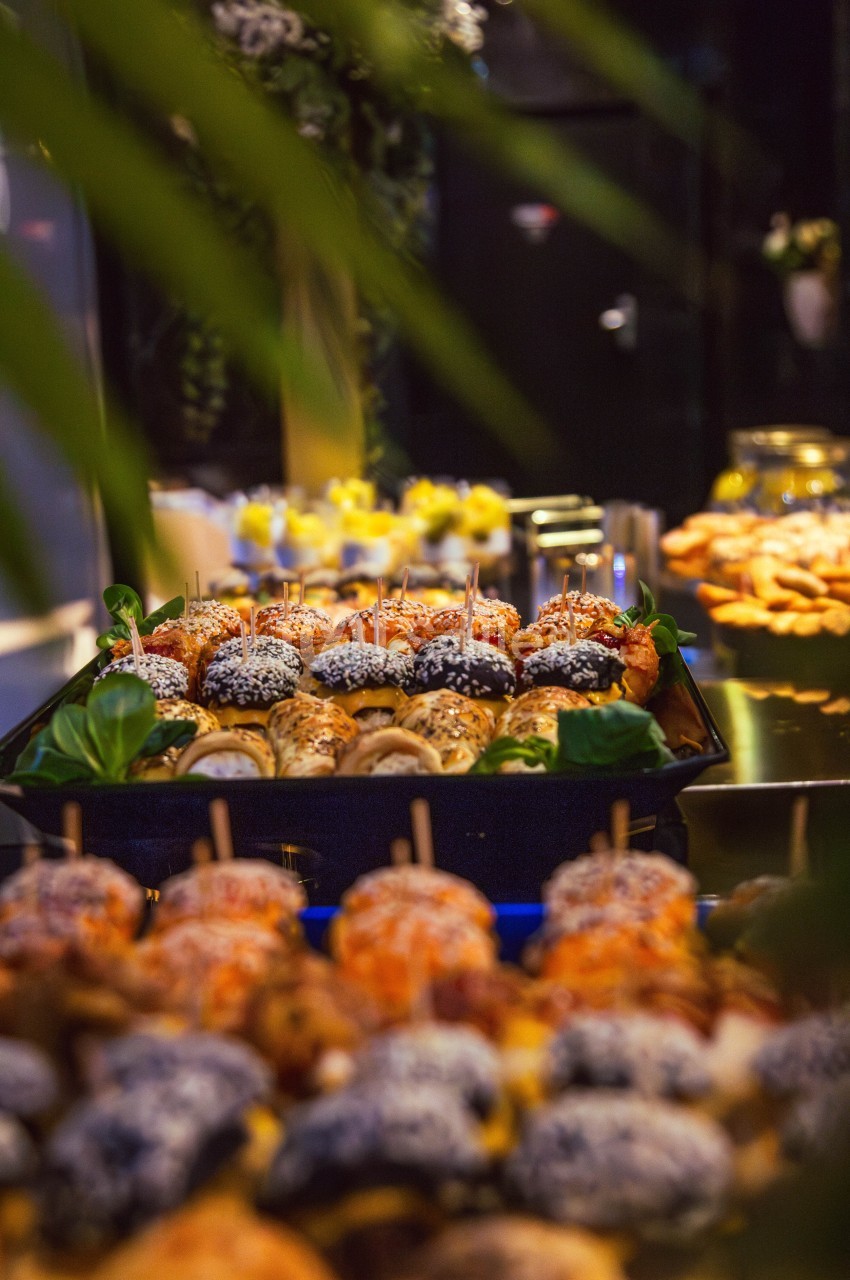 Plateau de bouchées apéritives variées, décorées de graines et herbes, présenté sur une table lors d'un buffet.