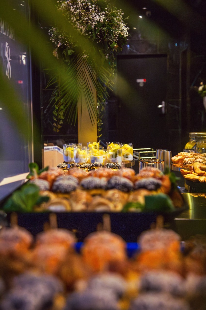 Buffet avec pâtisseries variées au premier plan et verrines de desserts en arrière-plan, décoré de feuillage.