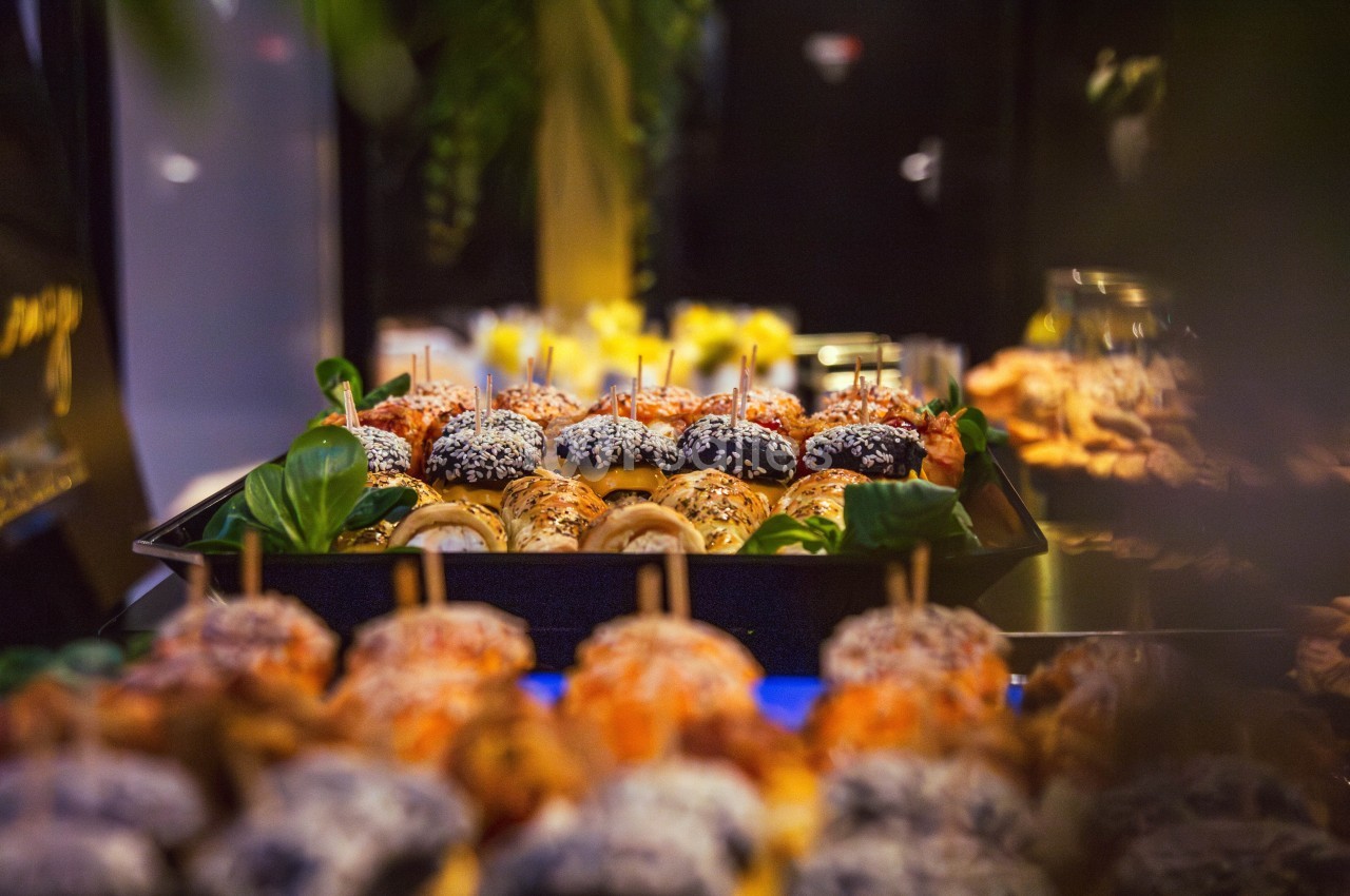 Plateau de mini-burgers variés garnis de graines et de légumes, présenté sur une table lors d'un buffet.