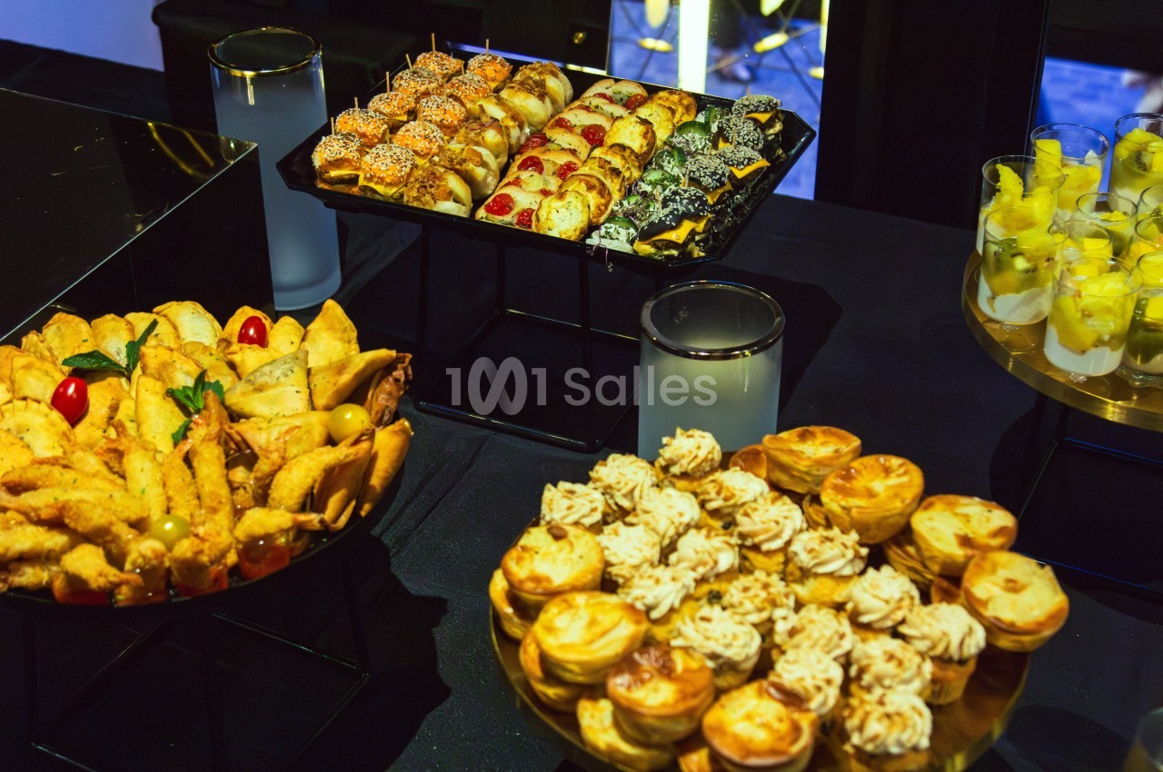 Plateaux de pâtisseries et amuse-bouches variés disposés sur une table noire lors d'un buffet.