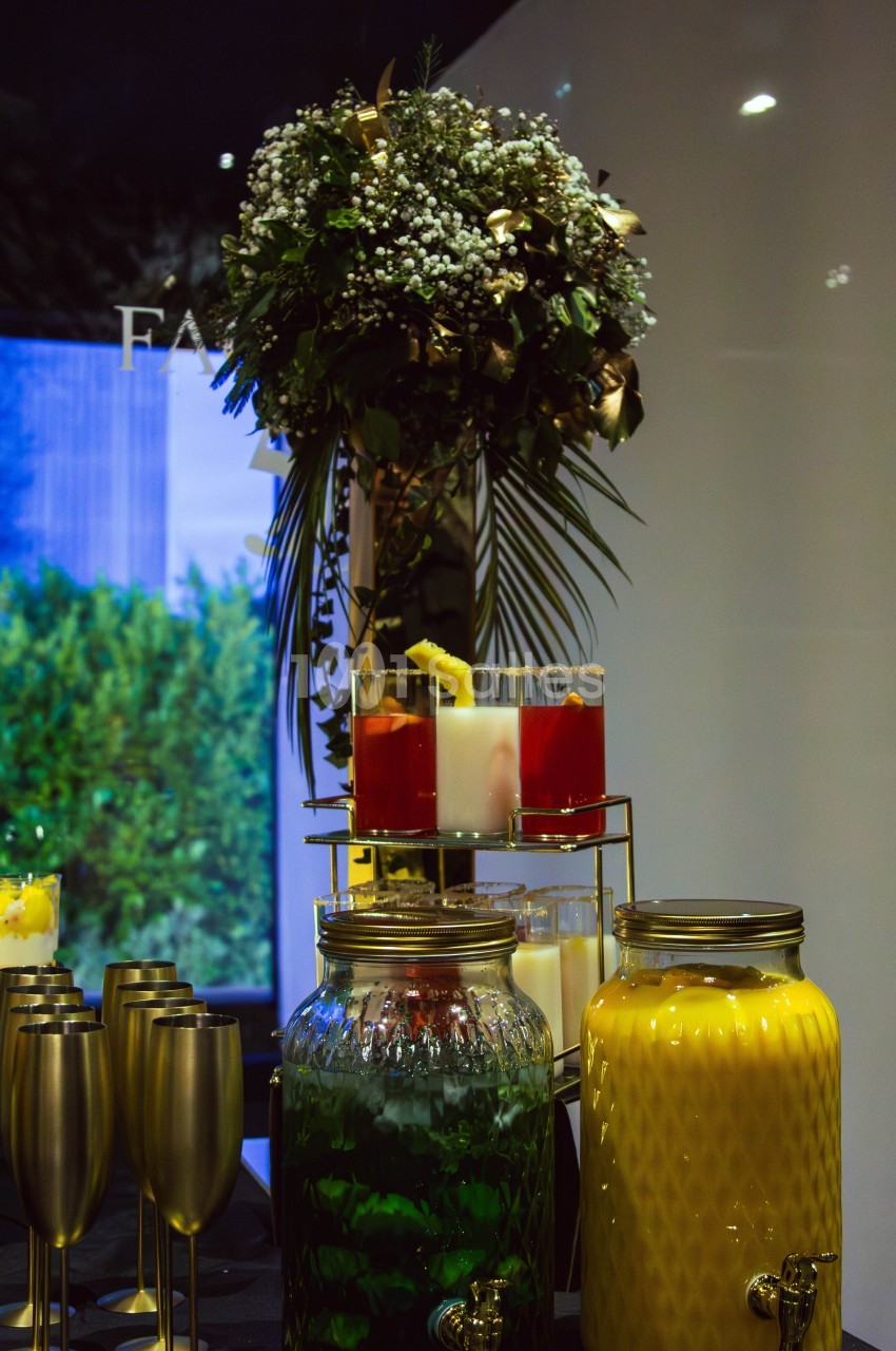 Buffet avec boissons colorées, verres dorés et une décoration florale en arrière-plan.