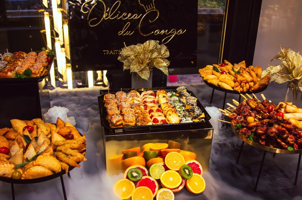 Plateau de buffet varié avec sushis, fruits frais, brochettes et assortiments de beignets, décoré de motifs dorés.
