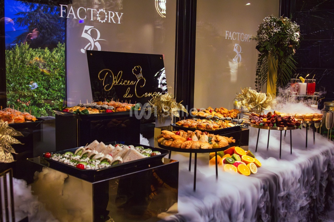 Buffet élégant avec plats variés, fruits et décorations, entouré d'une ambiance de fumée et d'éclairage tamisé.