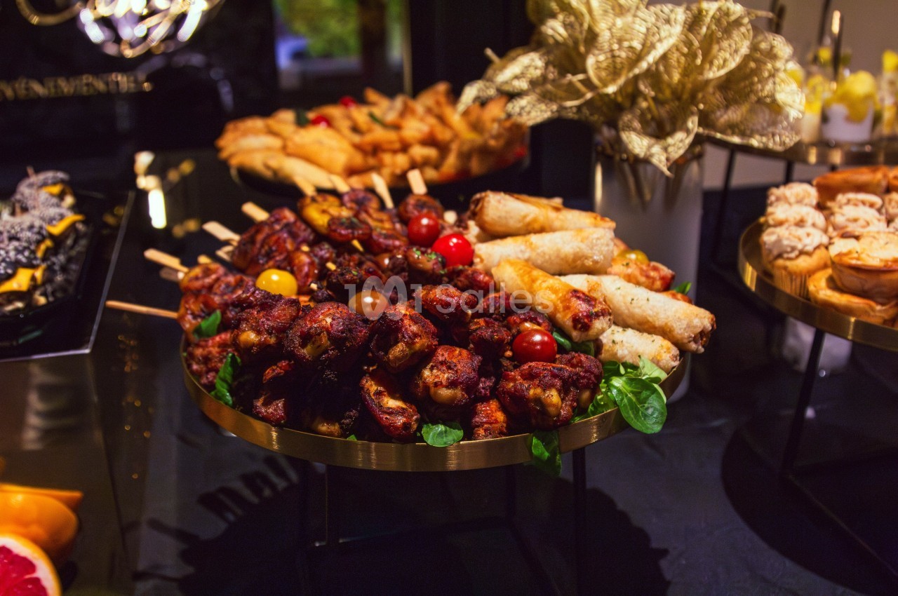 Plateau de brochettes de viande grillée, rouleaux croustillants et autres amuse-bouches sur une table de buffet.