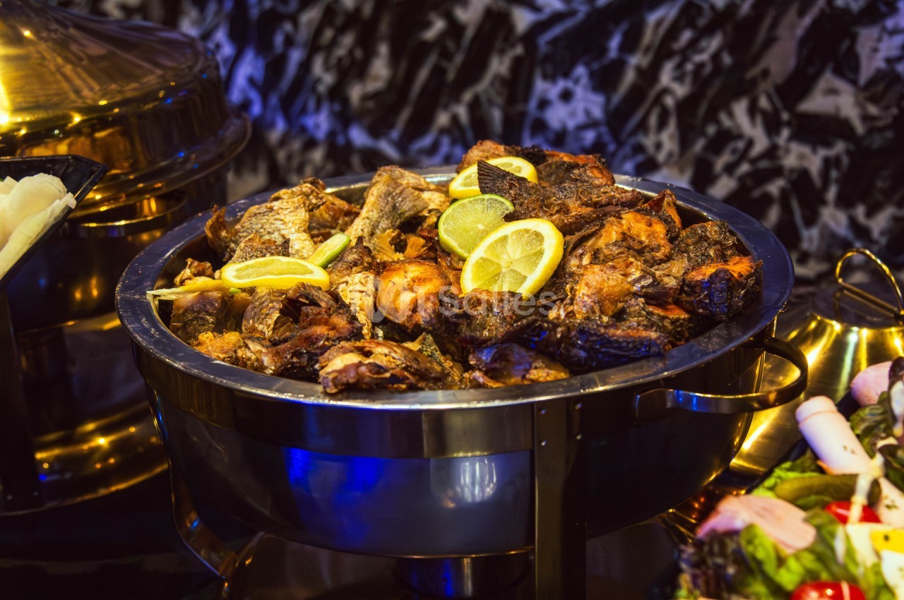 Plat de poissons grillés garnis de tranches de citron, présenté dans un récipient en métal sur une table.
