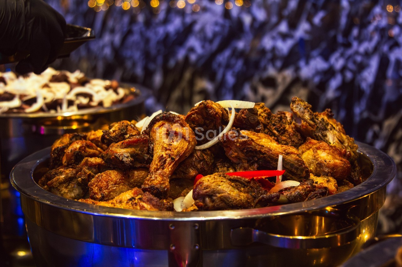 Poulet rôti assaisonné servi dans un plat en métal, décoré de rondelles d'oignon et de morceaux de piment rouge.
