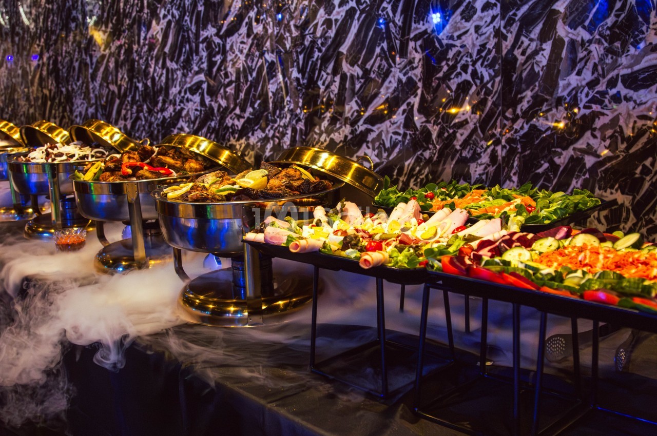 Buffet varié avec plats chauds dans des récipients en métal et salades fraîches sur des plateaux, décoré de fumée…