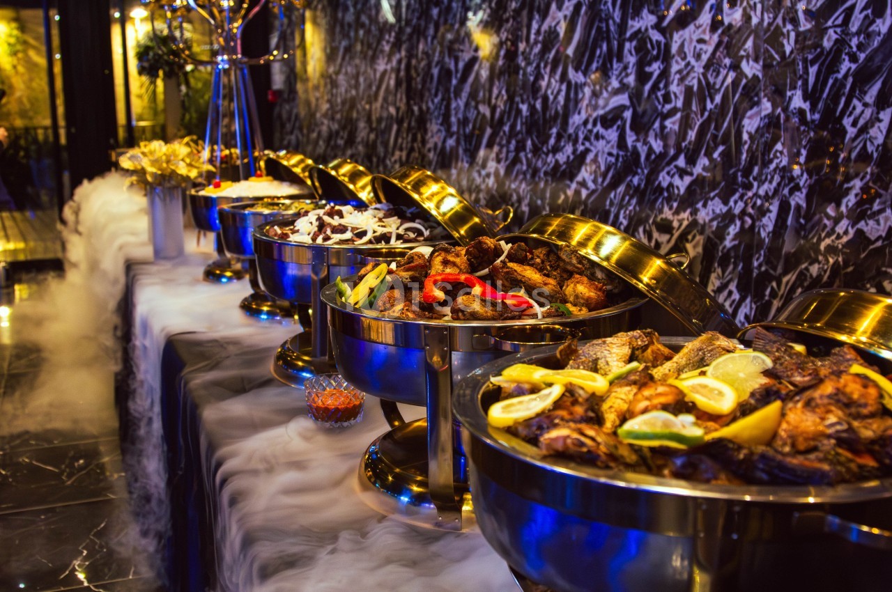 Buffet avec plusieurs plats chauds présentés dans des récipients en métal, entourés d'une légère fumée décorative.