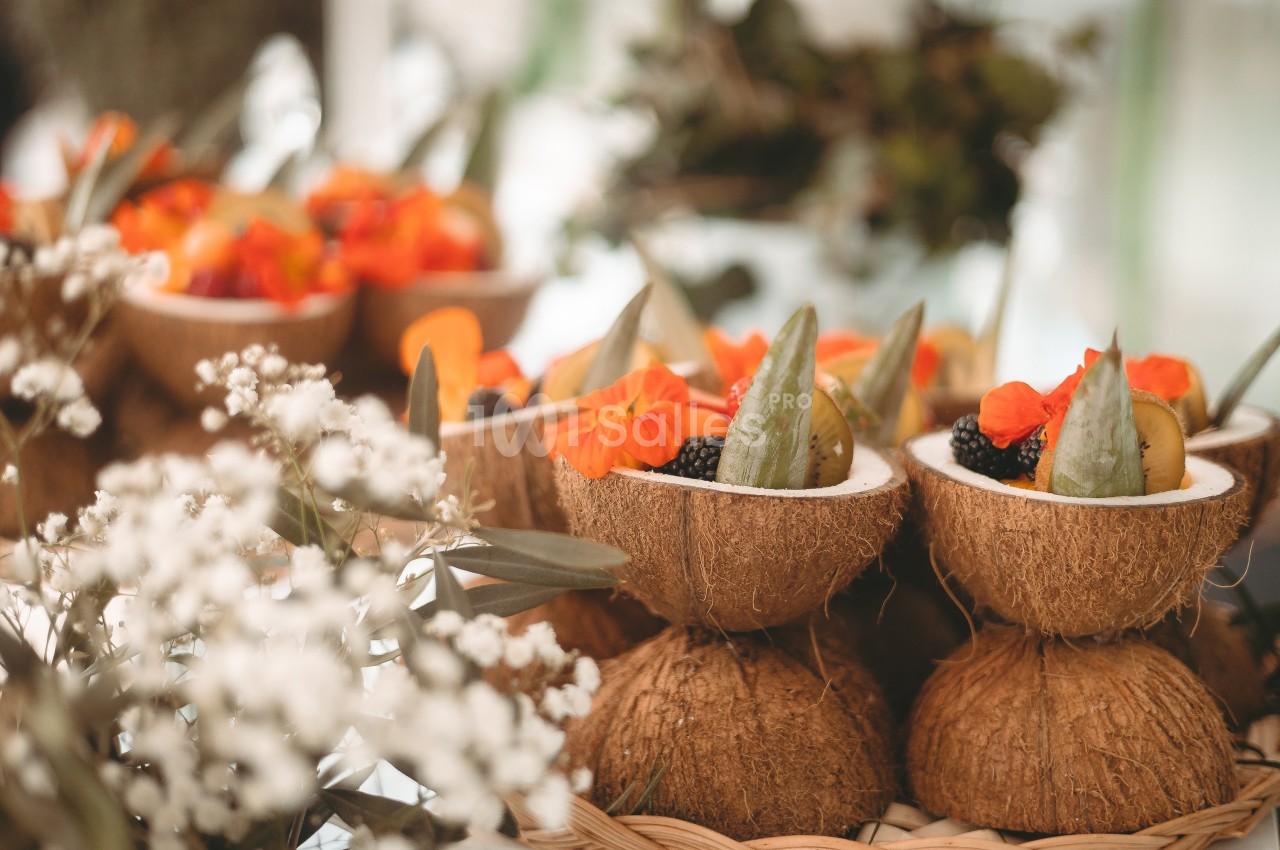 Moitiés de noix de coco remplies de fruits frais et décorées de fleurs orange, disposées sur une table.