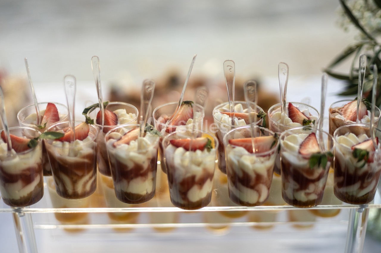 Verrines de dessert avec mousse blanche, coulis de fruits rouges et morceaux de fraises fraîches, présentées sur un plateau.