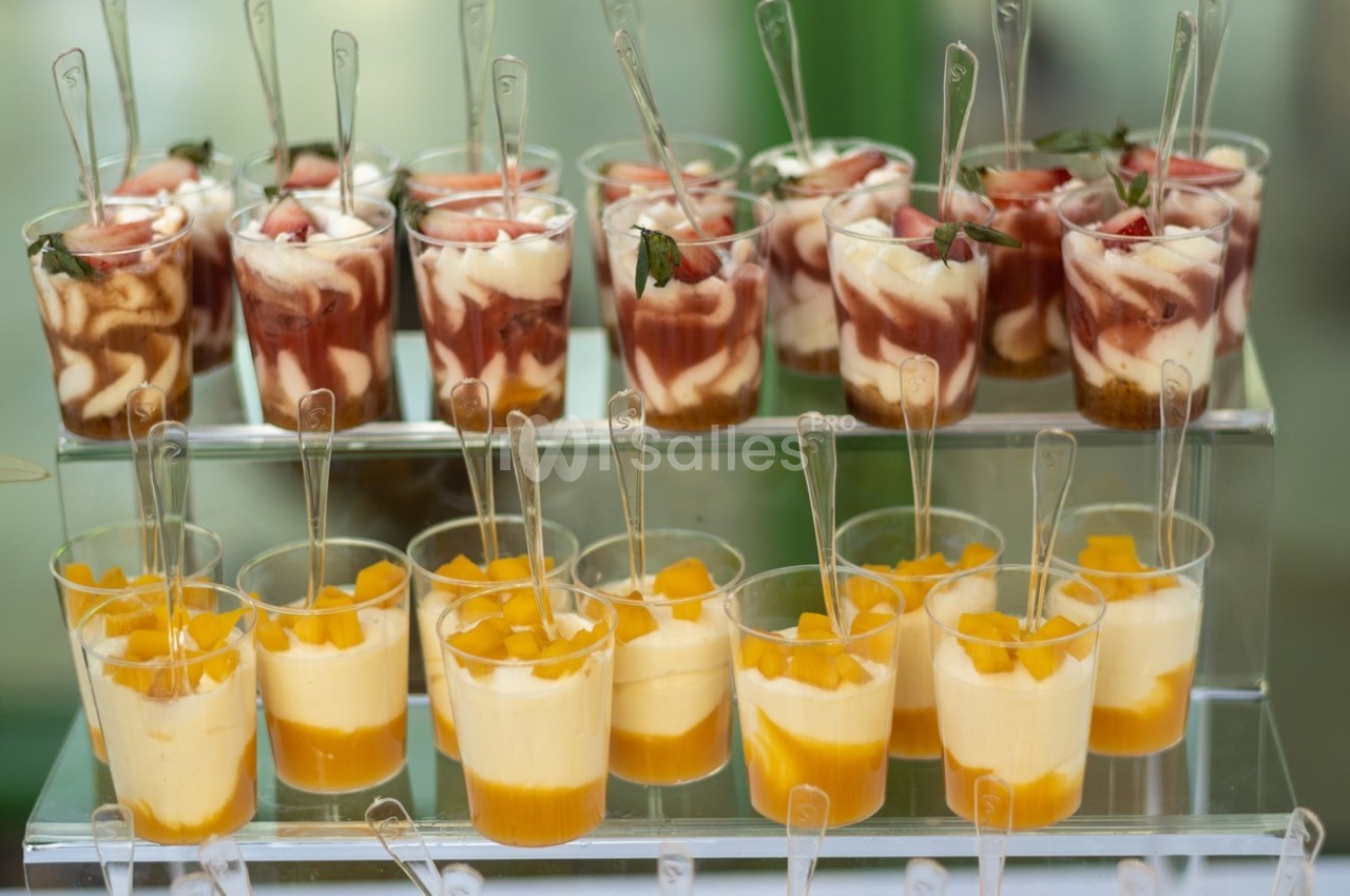 Desserts en verrines avec couches de fruits, crème et biscuits, présentés sur un présentoir transparent.